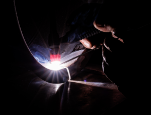 Welder performing pipeline welding while using a compact welding camera to monitor the weld inside a confined industrial environment